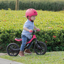 Niño con casco andando en la bicicleta de balance Globber Go Bike Elite Fuchsia en el pasto
